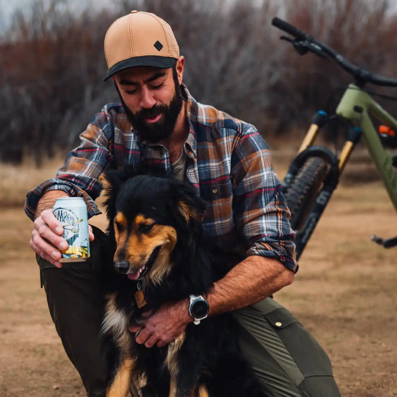 Man with a dog and a beer can in an outdoor setting with a bicycle in the background