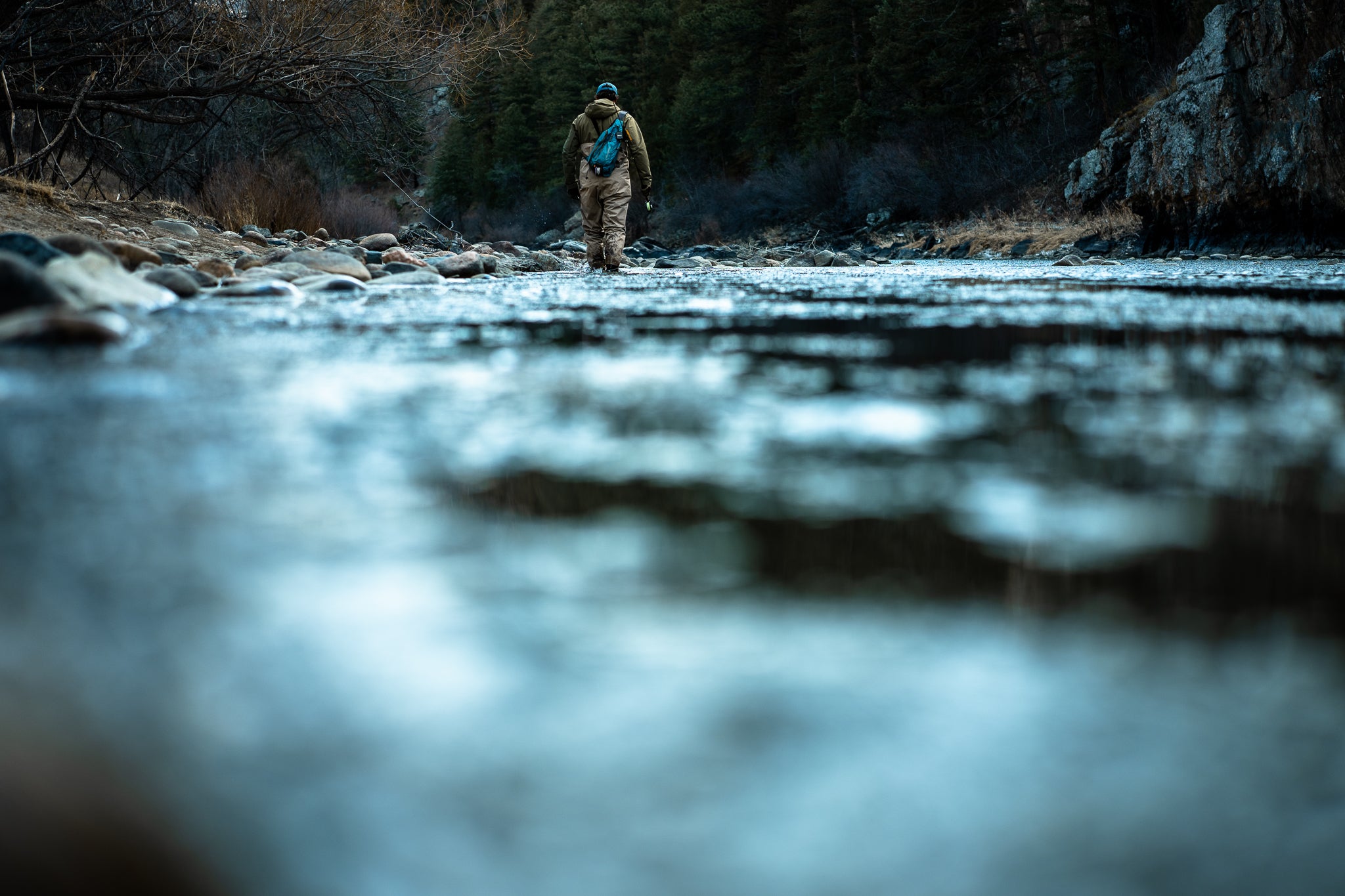 Fisherman in hat wading rocky river