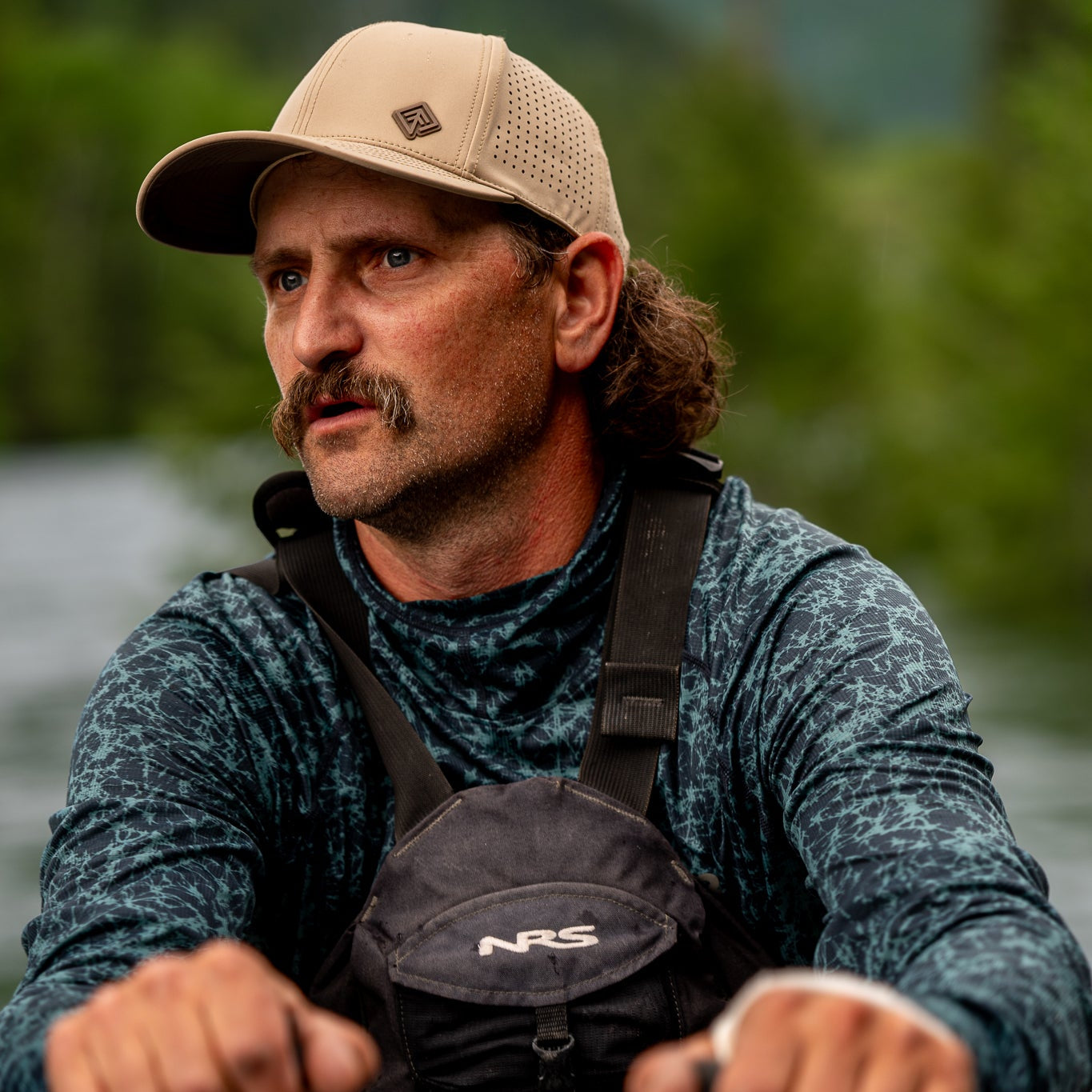 Man rowing a kayak wearing a cap and NRS life jacket on a body of water.