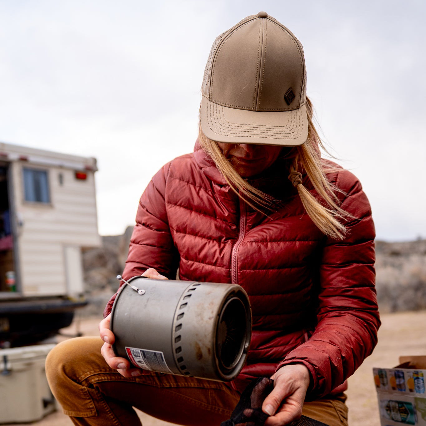 Person in red jacket and beige cap holding a cylindrical object outdoors.