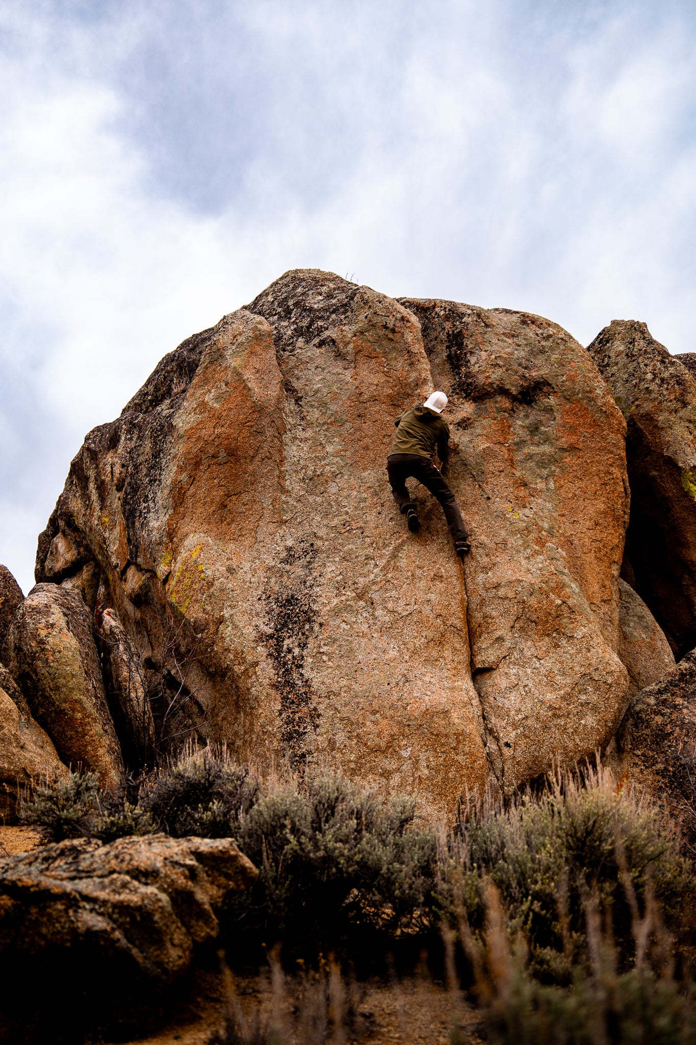 Rock climber in white hat scaling boulder
