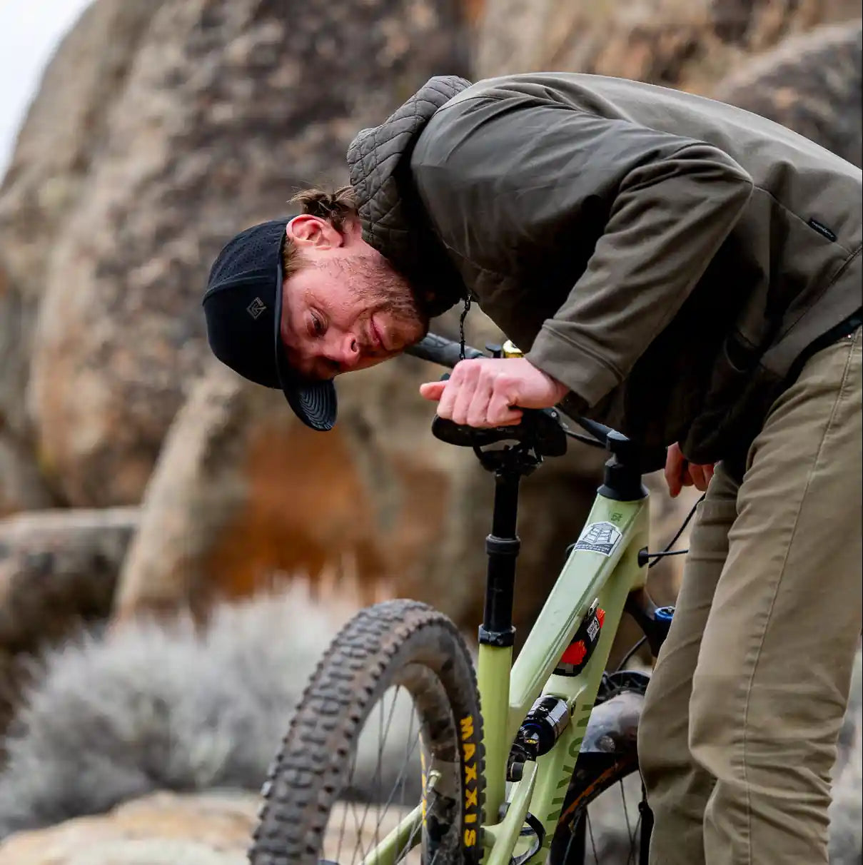 Man adjusting a mountain bike in a rocky outdoor setting