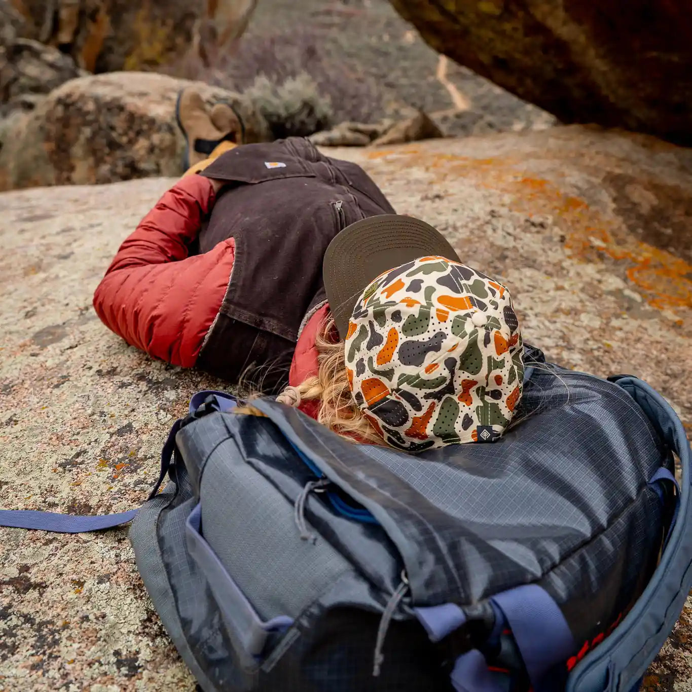 Person lying on a rock with a backpack, surrounded by rocky landscape
