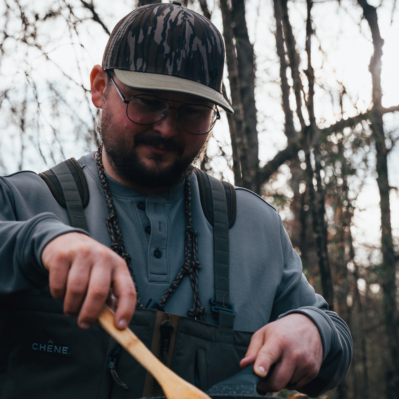 Person cooking outdoors in a forest setting with a backpack and camping stove.