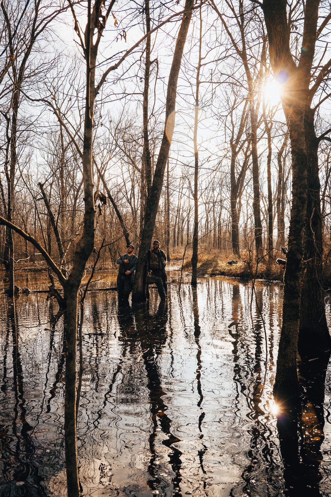 Two hat-wearing hunters wading flooded timber