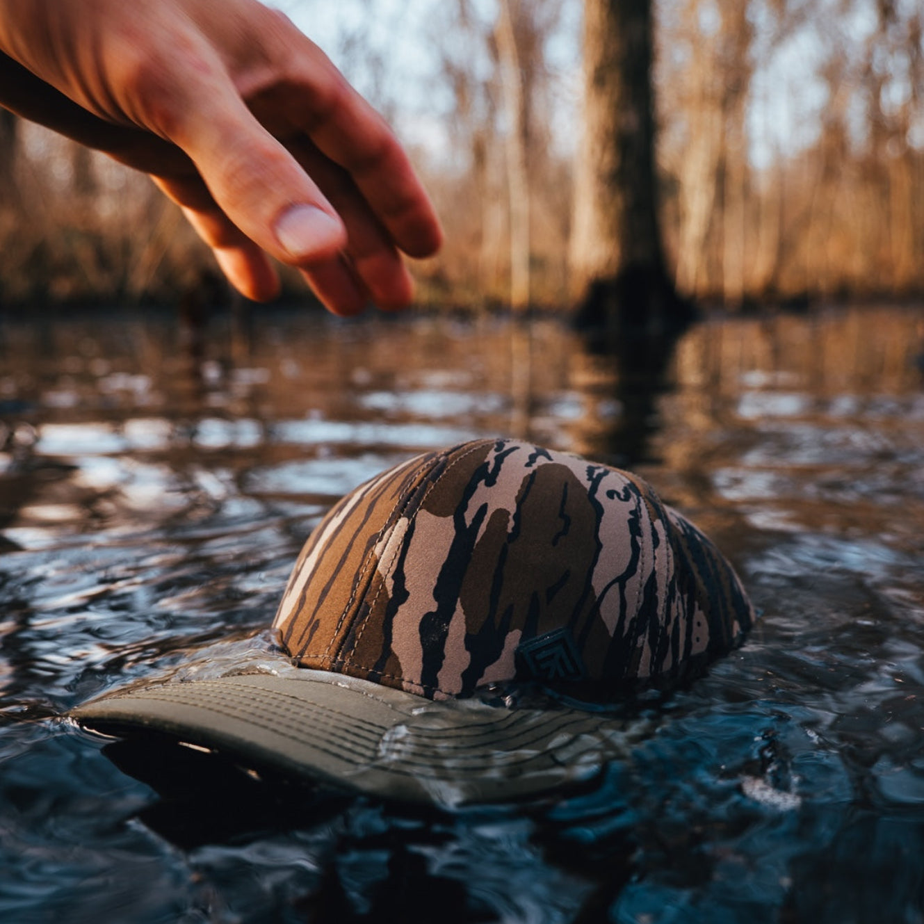 Hand reaching for camo hat floating water