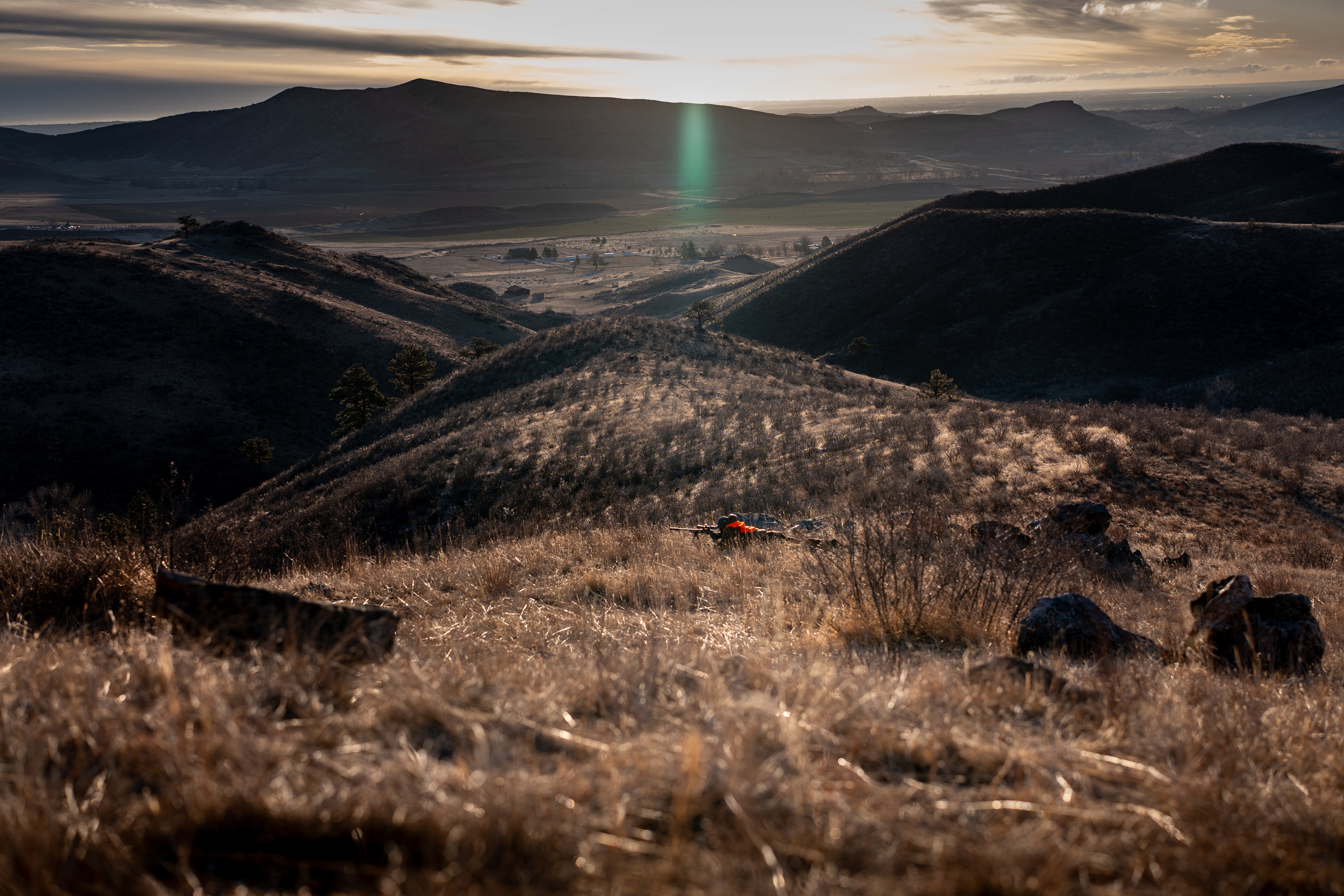 Hat-wearing hunter prone on mountain ridge
