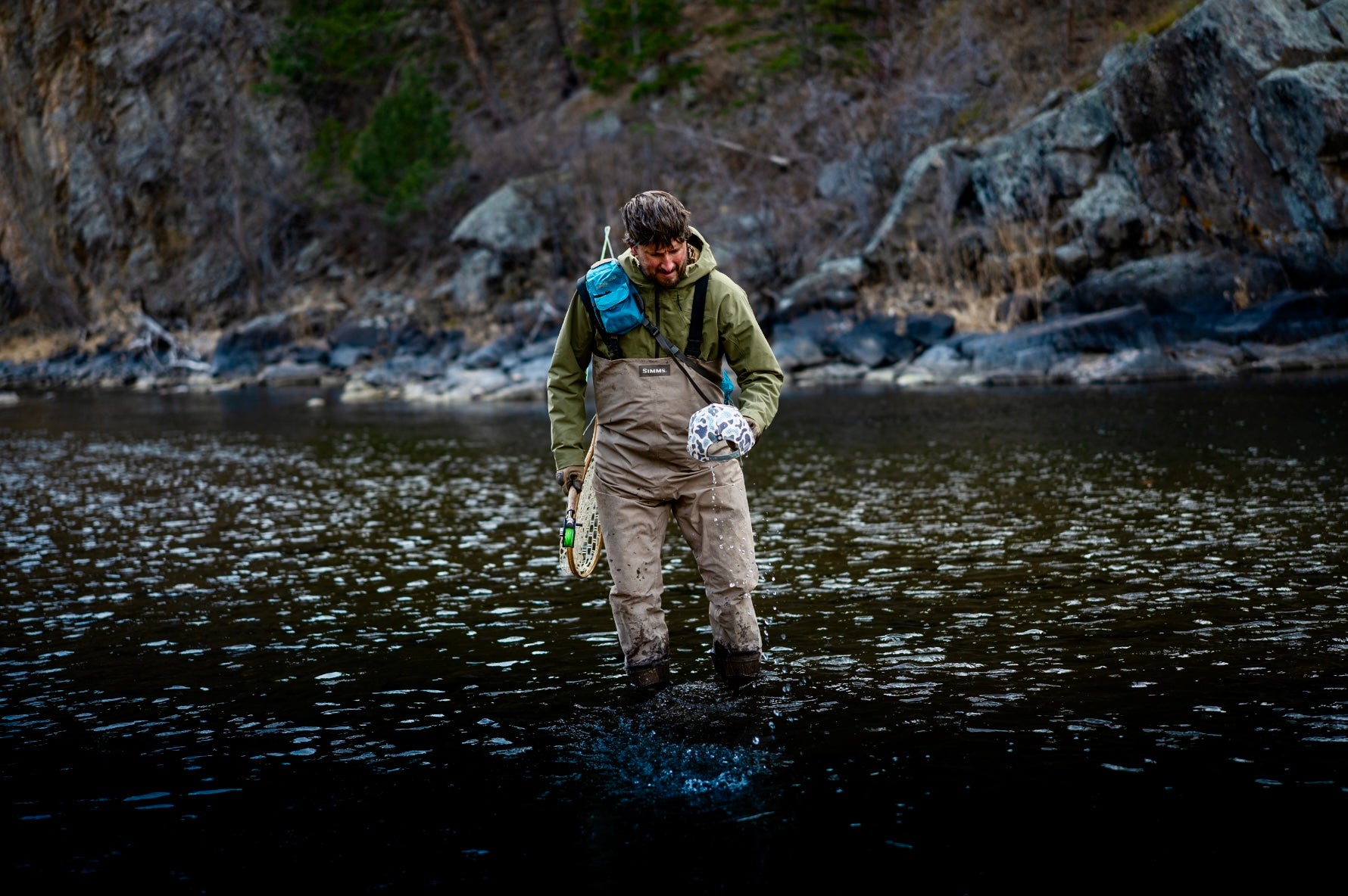 Fisherman wading river holding camo hat
