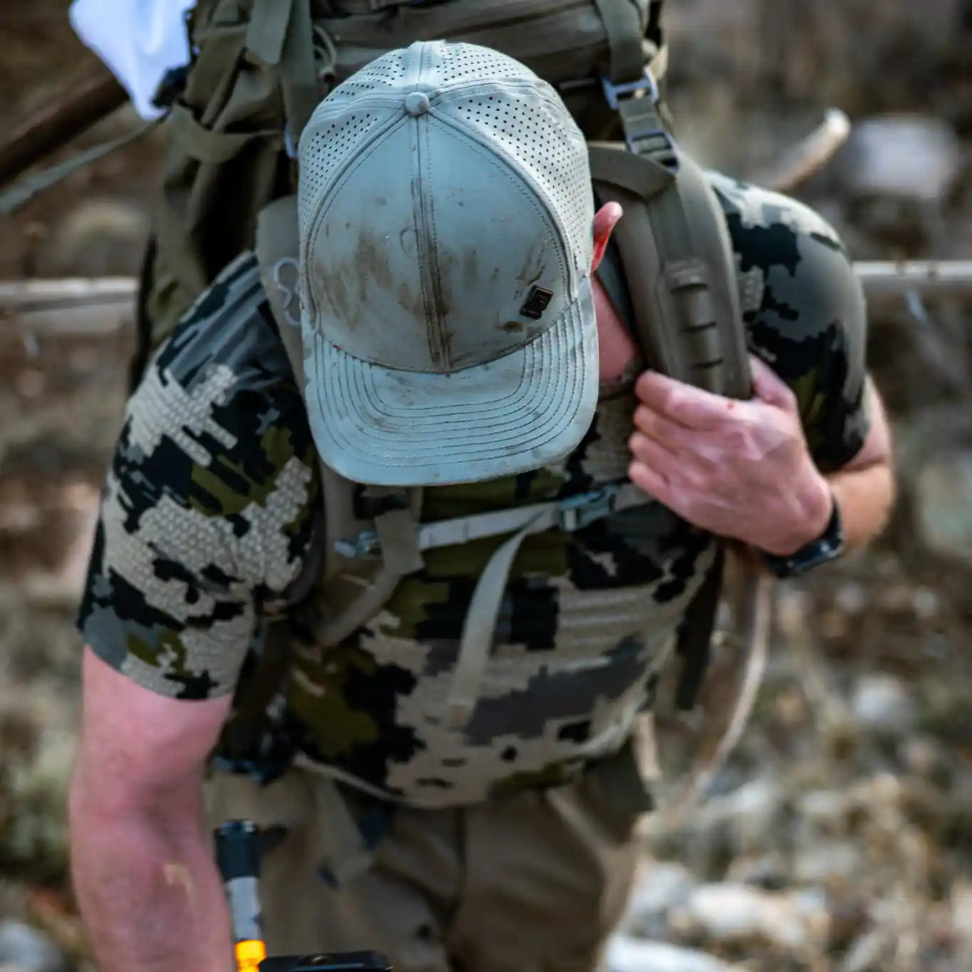 Person in camouflage gear with a backpack and archery bow in a natural setting