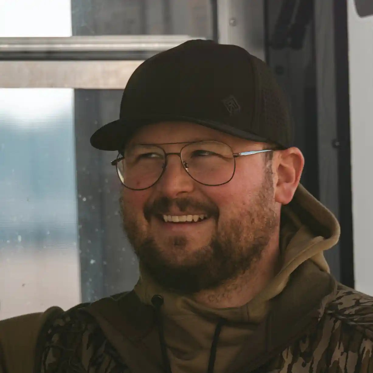Man wearing a cap and glasses, standing in front of a vehicle with visible branding.