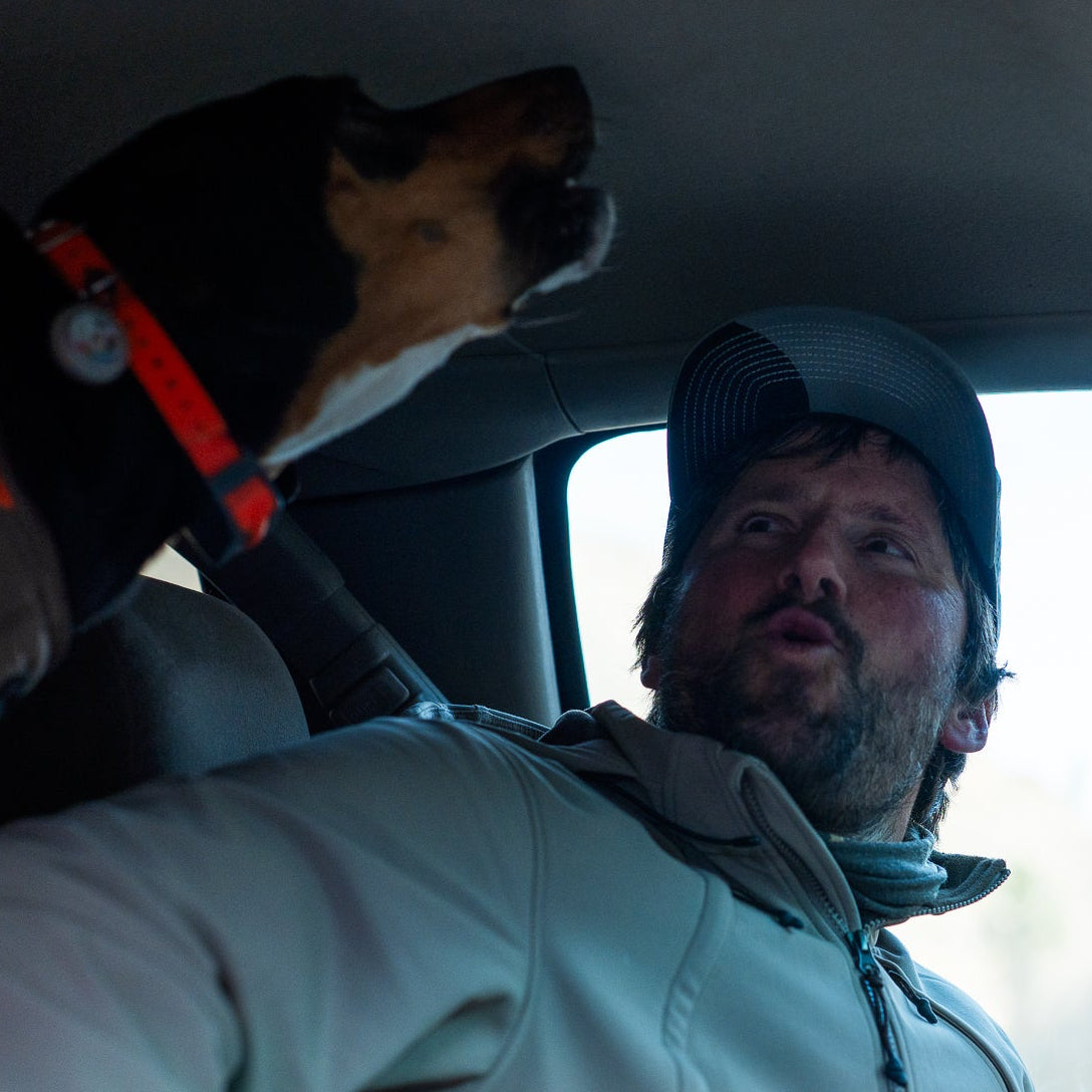 Man sitting in a car with a dog on his lap, looking out the window.
