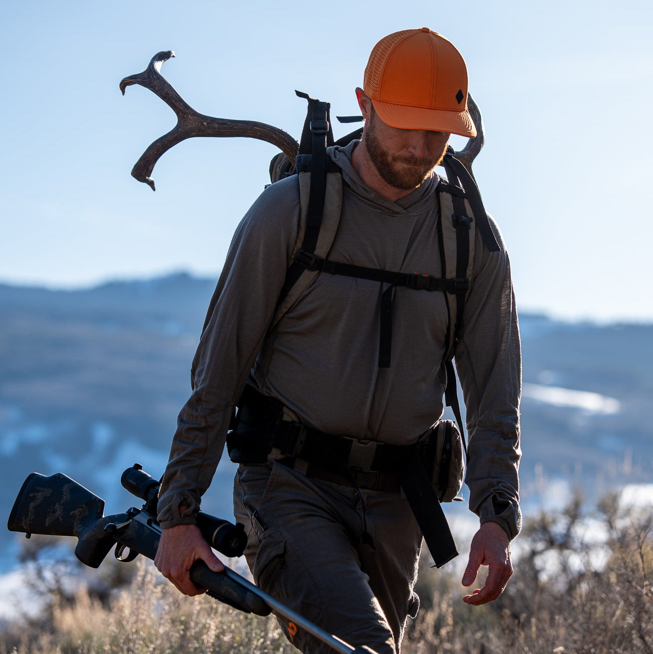Man in hunting gear with rifle and backpack in a mountainous landscape